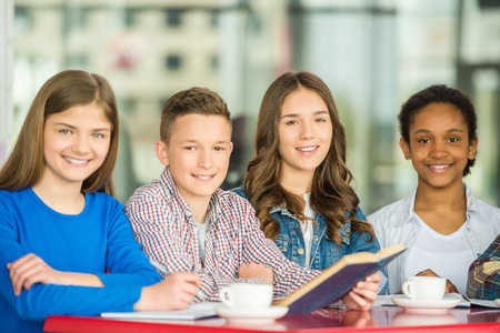 A group of teenagers sitting at the table in cafe, studying and drinking tea.の写真素材