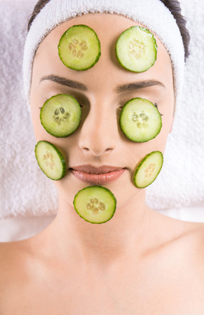 Young beautiful woman holding cucumber slices on the face in a spa salon.の写真素材