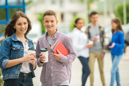 Two smiling cheerful teenagers drinking coffee at park after lessons.の写真素材