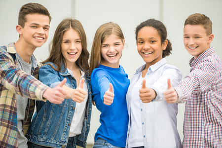 Group of smiling cheerful teenagers having fun after lessons and showing thumbs up.の写真素材