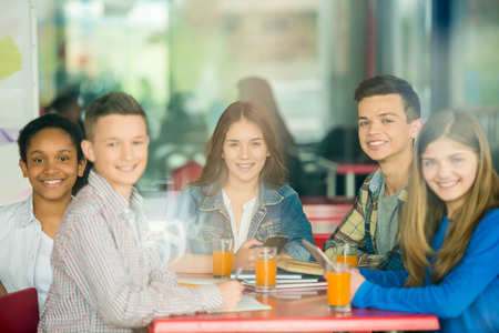 A group of teenagers sitting at the table in cafe, studying and drinking orange juice. Image through a glass.の写真素材