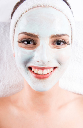 Young beautiful woman holding mask on the face in a spa salon.の写真素材