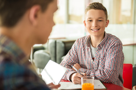 Male teenager sitting in cafe with friends, studying and drinking orange juice.の写真素材