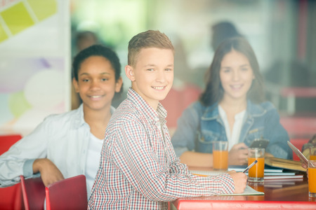 A group of teenagers sitting at the table in cafe, studying and drinking orange juice. Image through a glass.の写真素材