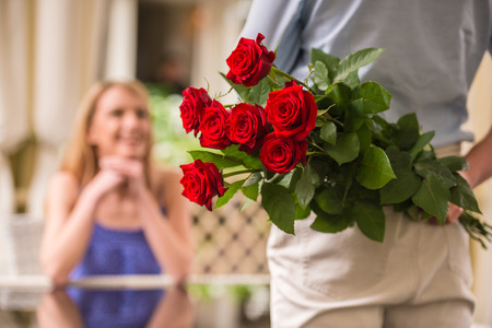 Young woman looking at man with flower bouquet behind the back.の写真素材
