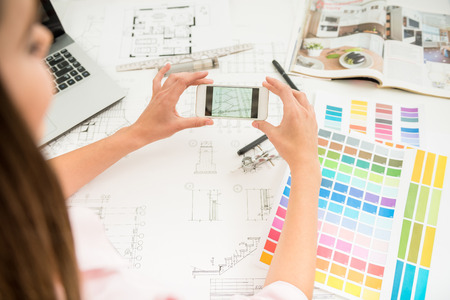 Young beautiful designer working in her modern home office and using phone.の写真素材
