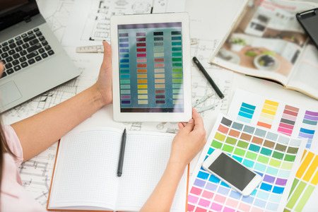Close-up of  designer holding digital tablet in hands and working with color samples.