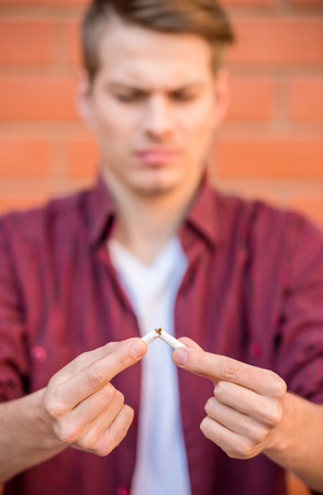 Handsome young man in smart casual wear, breaking cigarette outdoors.の写真素材