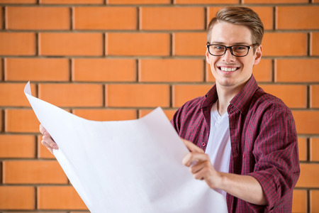 Young man in glasses holding paper whatman. Brick wall background.の写真素材