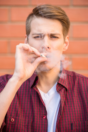 Handsome young man in smart casual wear, smoking cigarette outdoors.の写真素材