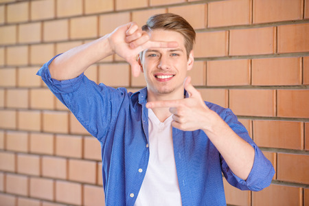Handsome young man in smart casual wear showing frame gesture on brick wall background.の写真素材
