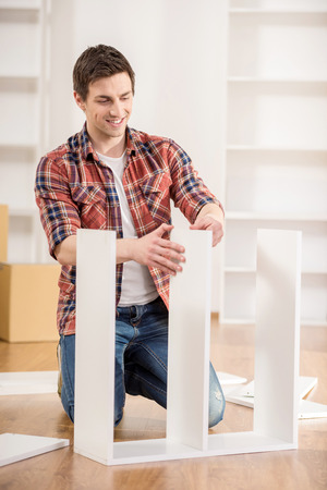Young man dressed casual assembling furniture in new house.の写真素材
