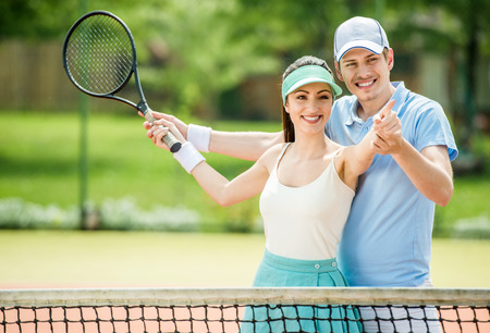 Smiling young couple standing on tennis court, holding tennis racket.の写真素材