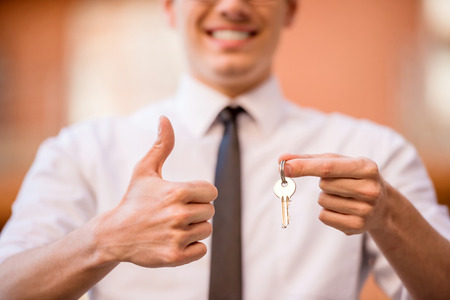 Successful realtor in white shirt showing key and making thumb up at camera.の写真素材