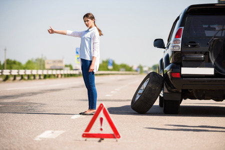 Red warning triangle with a broken down car on the road. Woman catching car.の写真素材