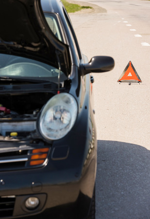 Red warning triangle with a broken down car on the road.の写真素材