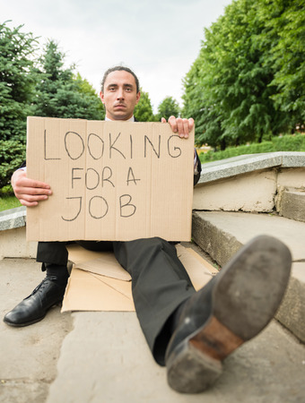 Man in suit sitting at stairs with sign. Unemployed man looking for job.
