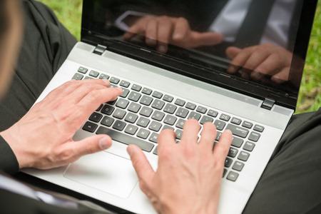 Close-up of man in suit sitting at lawn with laptop.の写真素材