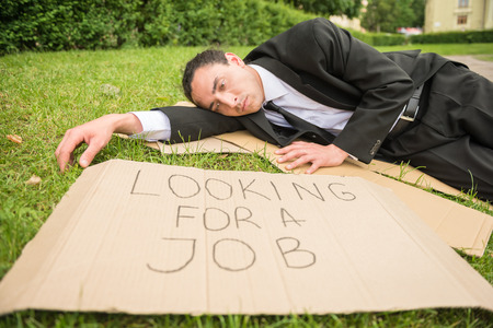 Frustrated unemployed man with sign lying down the lawn.の写真素材
