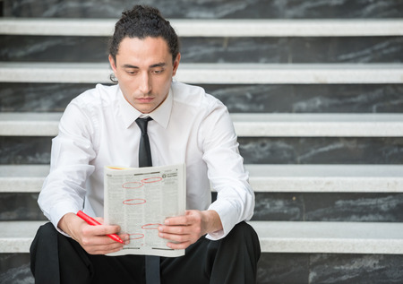Man in suit sitting at stairs with  newspaper and searching job.の写真素材