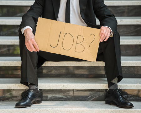 Close-up of man in suit sitting at stairs with sign in hands. Unemployed man looking for job.の写真素材