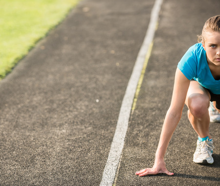 Attractive sporty girl ready to run sprint. Female athlete in powerful starting line pose.