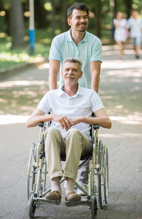 Adult son walking with disabled father in wheelchair outdoor. Front view.の写真素材