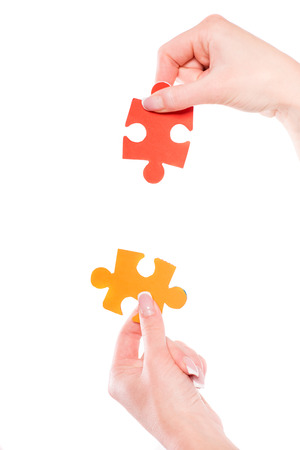 Close-up of hands trying to connect small jigsaw puzzles over white background.の写真素材