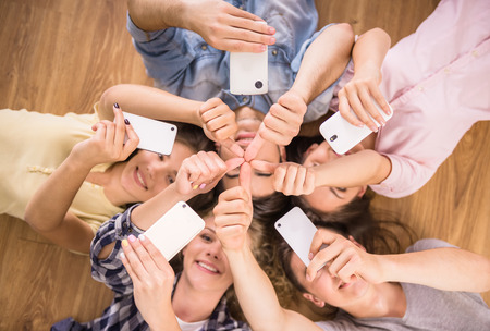 Education, people and technology concept - close up of students or friends with smartphones lying on floor in circle.の写真素材