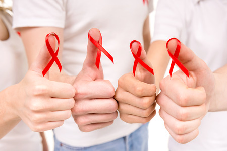 Close-up of hands holding red ribbons to rise AIDS HIV awareness.