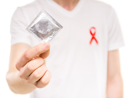 Healthcare and medicine concept - man with red AIDS awareness ribbon with condom in hand.の写真素材