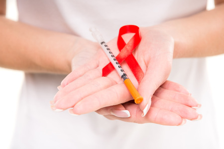 Healthcare and medicine concept - female hands holding red AIDS awareness ribbon.