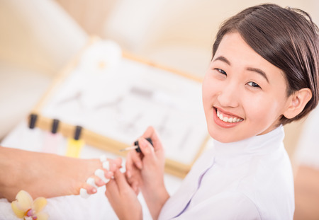 Close-up of pedicurist applying nail polish to the toenails.の写真素材