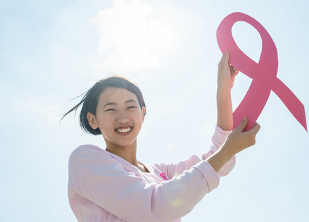 Woman showing pink ribbon to support breast cancer, sky background.の写真素材