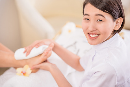 Smiling asian pedicurist working with client at spa. Foot care concept.の写真素材