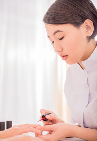 Pretty asian manicurist applying nail polish to client. Hands care concept.の写真素材