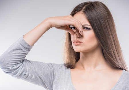 Beautiful young lady covers nose with hand showing that something stinks.の写真素材