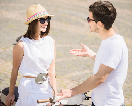 Nifty young couple talking to each other and smiling while woman sitting on scooter. Weekend together.の写真素材