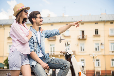 Beautiful young couple dressed casual sitting on scooter together. Side view.の写真素材