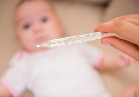 Mom checks the temperature of ill little baby.