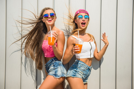 Beautiful female friends with juice are having fun against the wall, outdoor.