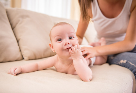 Young mom and little baby playing on the bed at home.