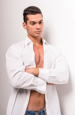 Young muscular man with perfect torso in opened shirt is standing on white background.の写真素材