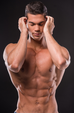 Bodybuilder man with perfect body, shoulders, biceps, triceps and chest, standing on black background with closed eyes.の写真素材