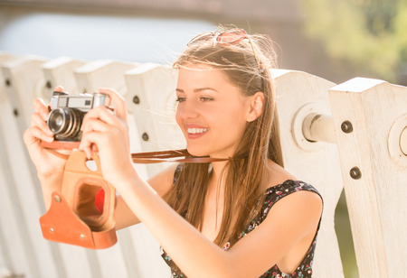 Smiling young woman is taking a picture with old camera, outdoors.の写真素材