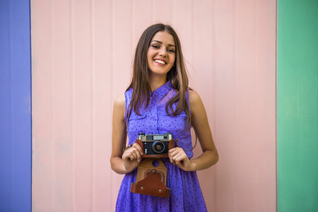 Young beautiful woman with old-fashioned camera standing against colorful wall.の写真素材