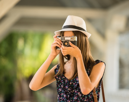 Young beautiful woman in hat is taking picture with old fashioned camera, outdoors.の写真素材
