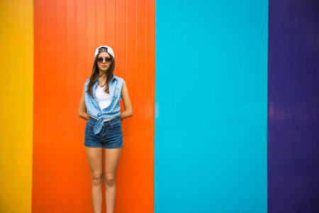 Pretty cool girl in sunglasses and cap standing against the colorful wall.の写真素材