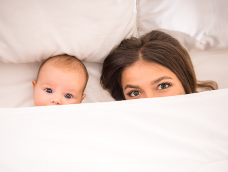Portrait of happy young mother with a baby in the bed at homeの写真素材