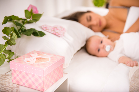 Gift box and rose for his lovely, in the background beautiful woman is sleeping with her cute babyの写真素材